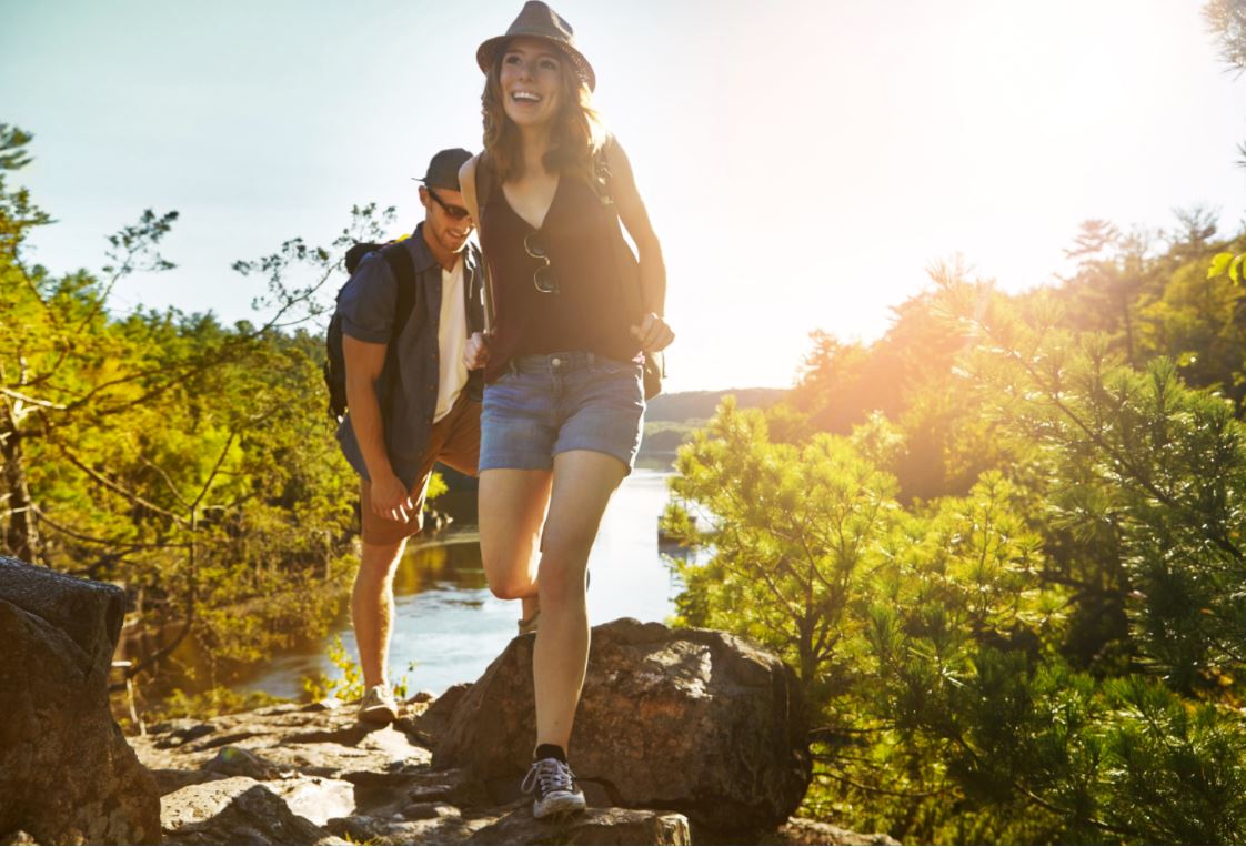 Two people wearing hats walking on a rocky path beside a lake.